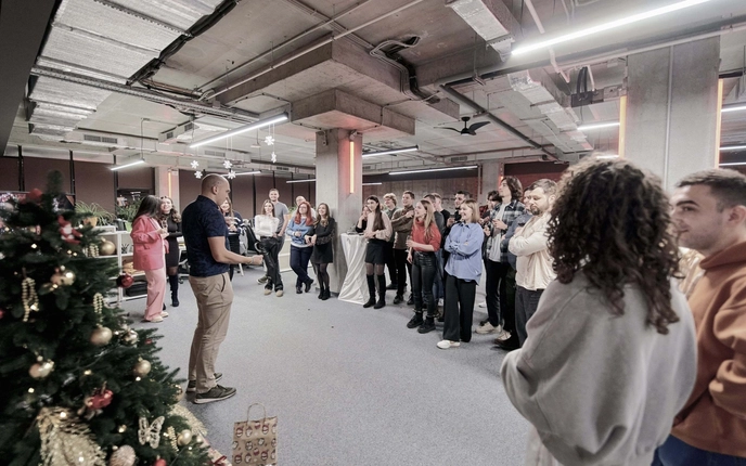 Person speaking to a group of people at an indoor holiday event with a decorated Christmas tree.