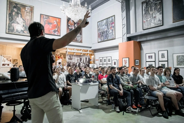 A speaker addressing a large audience during a presentation in an art gallery
