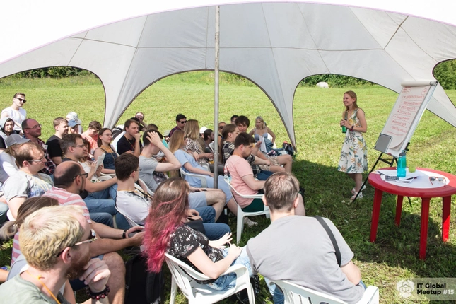 Outdoor presentation at IT Global Meetup with attendees seated under a tent.