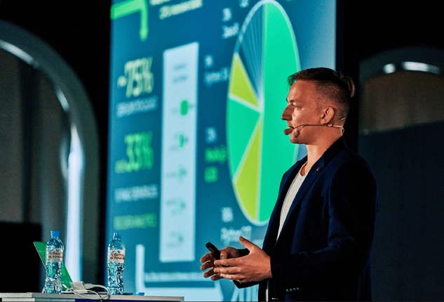 Speaker presenting data insights on stage with charts displayed on a screen.