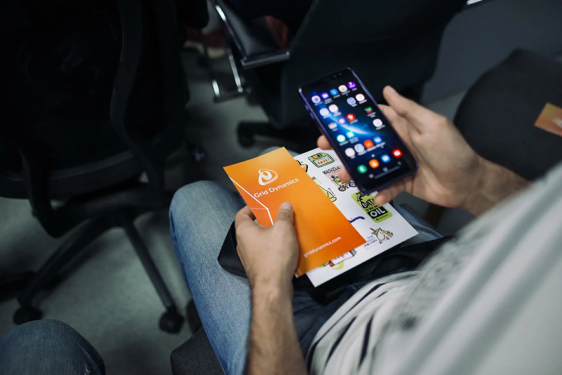 Person holding a Grid Dynamics pamphlet and using a smartphone.