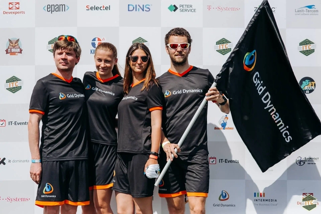 Four Grid Dynamics team members in black jerseys, posing with a company flag.