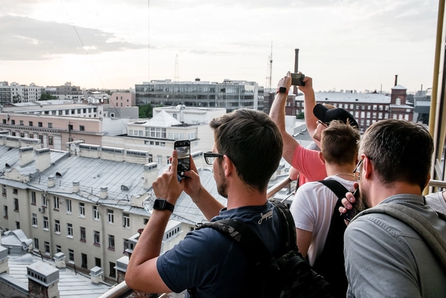 Group of people taking photos of a cityscape from a rooftop.