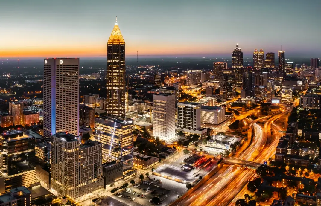 Skyline of Atlanta, Georgia at dusk featuring the iconic Bank of America Plaza, surrounded by busy highways and other city skyscrapers.